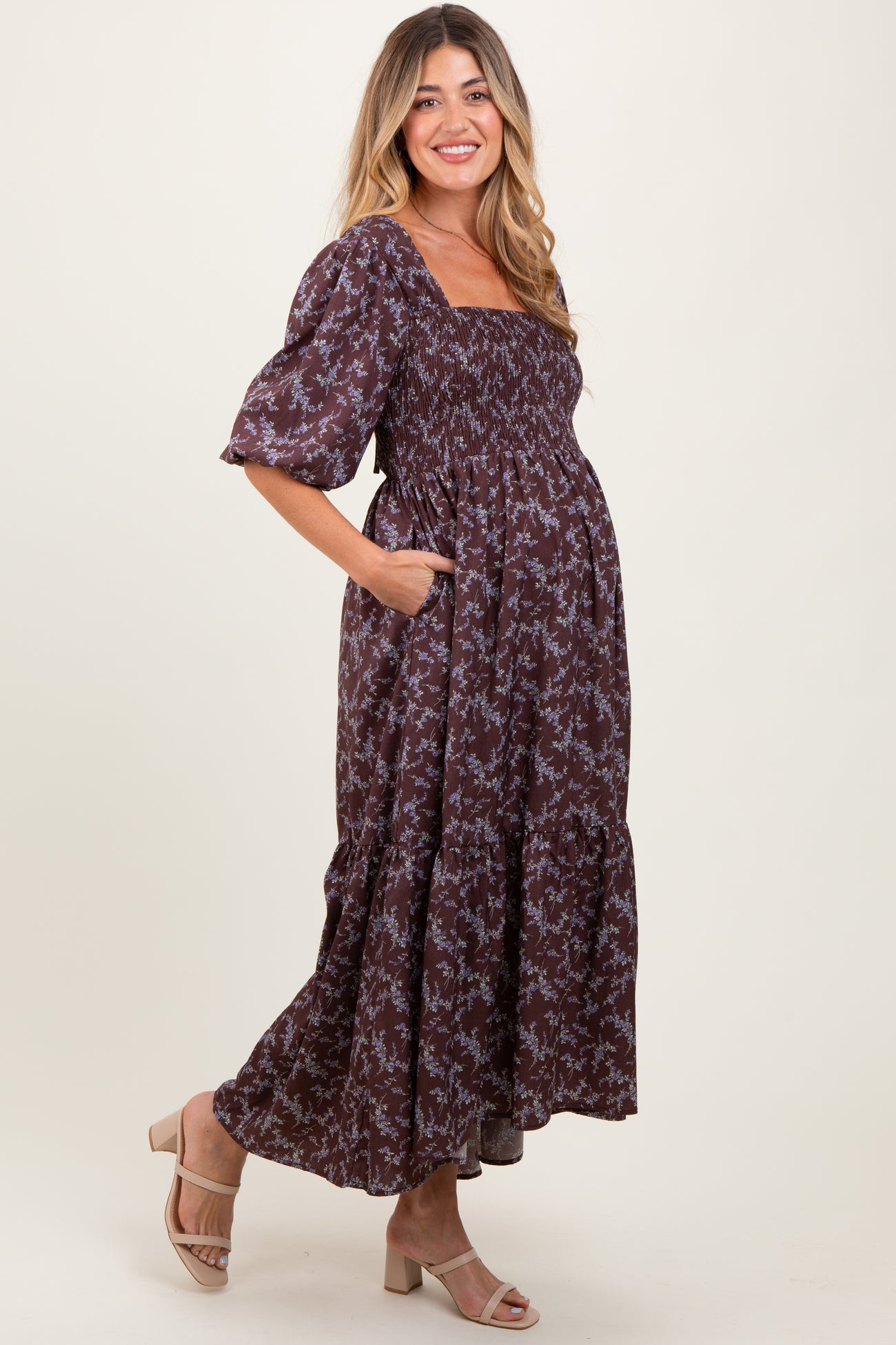 woman wearing a chocolate brown floral print maternity maxi dress with smocked bodice and puff sleeves, showing her baby bump