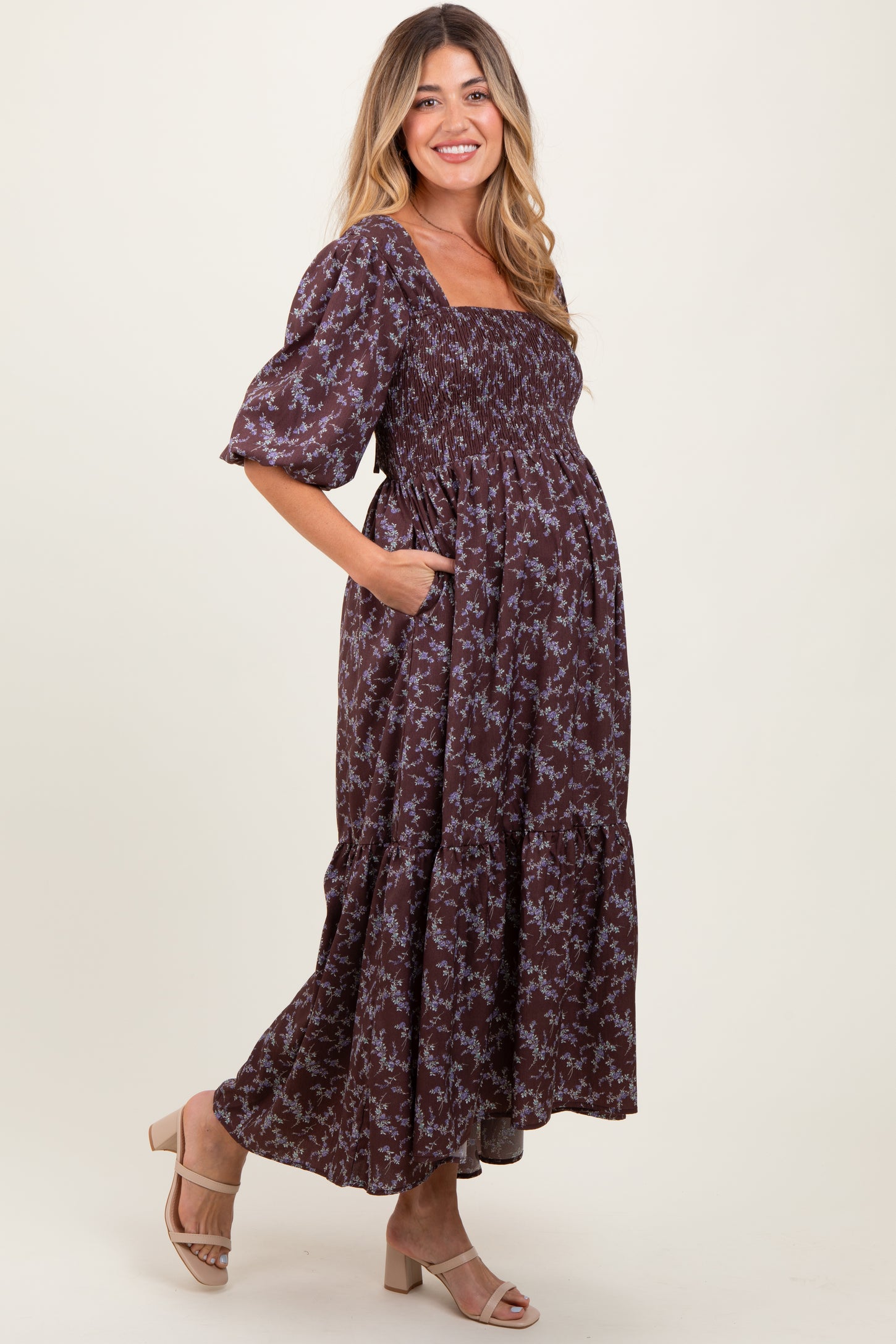 woman wearing a chocolate brown floral print maternity maxi dress with smocked bodice and puff sleeves, showing her baby bump