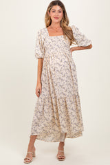 woman wearing a light beige floral maternity dress with puff sleeves and tiered skirt, showcasing her baby bump