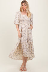 woman wearing a beige floral maxi dress with puff sleeves and a smocked bodice, standing with one hand in the pocket