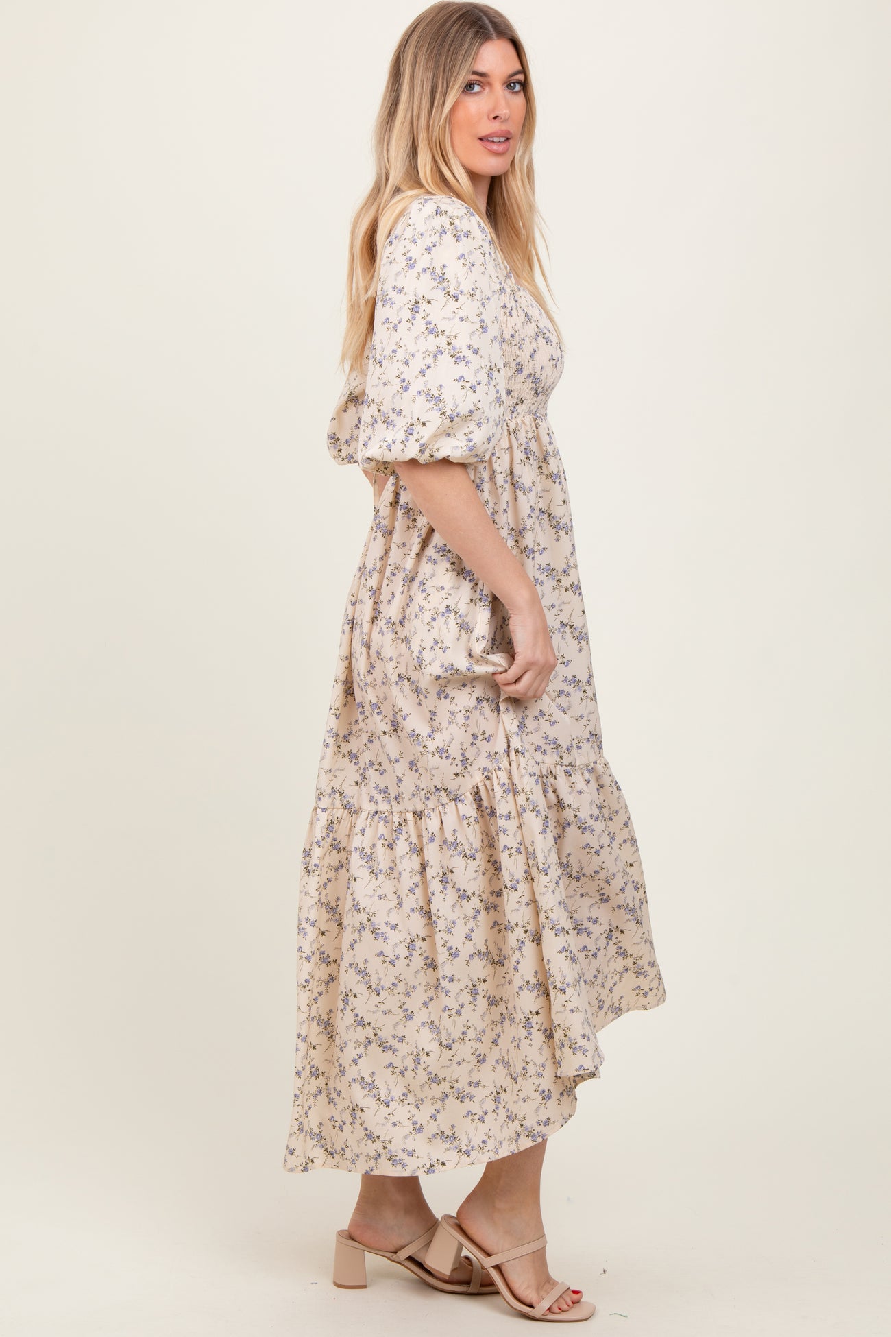 woman wearing a cream floral maxi dress with puff sleeves and a tiered hem, standing sideways