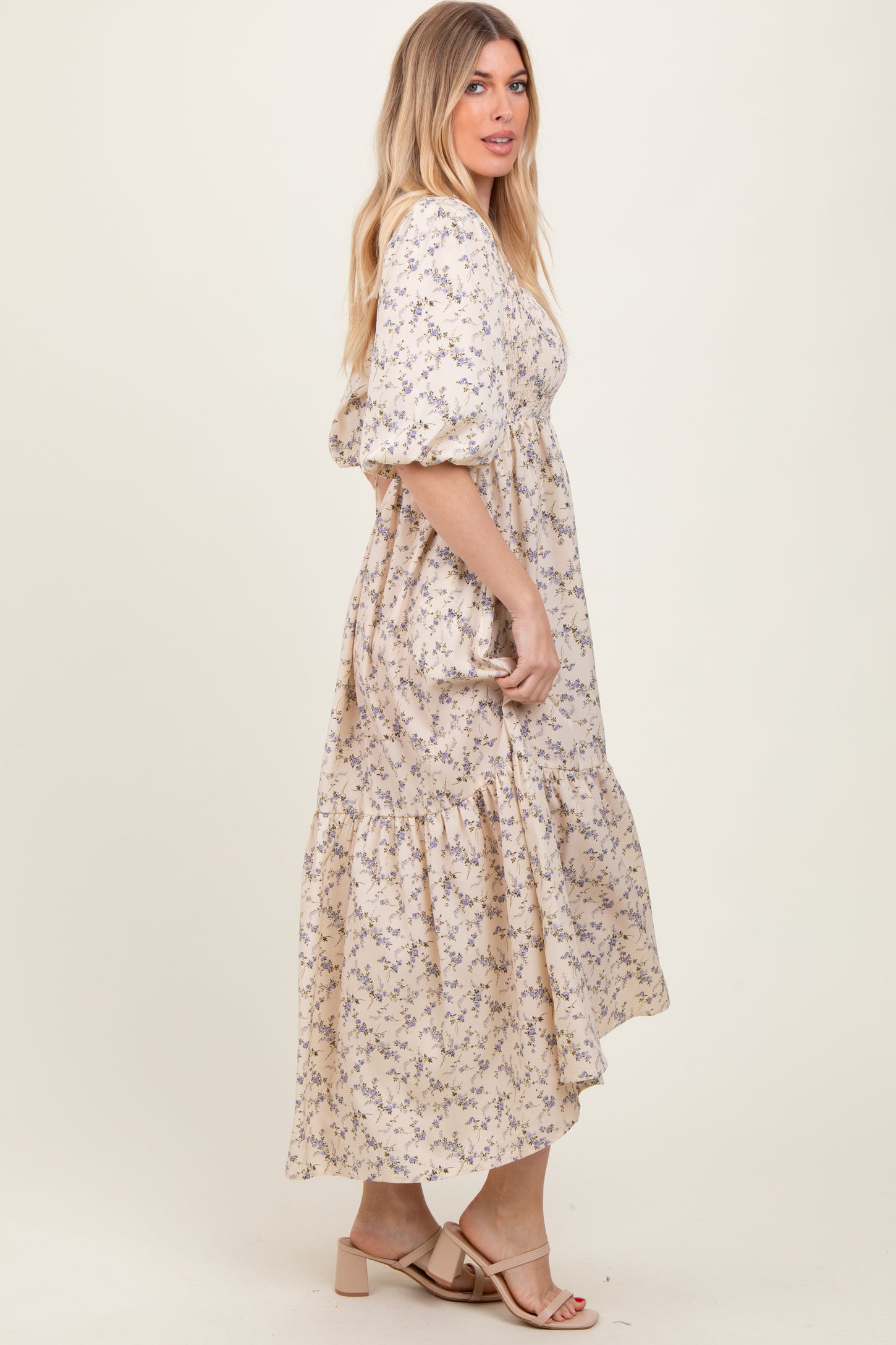 woman wearing a cream floral maxi dress with puff sleeves and a tiered hem, standing sideways