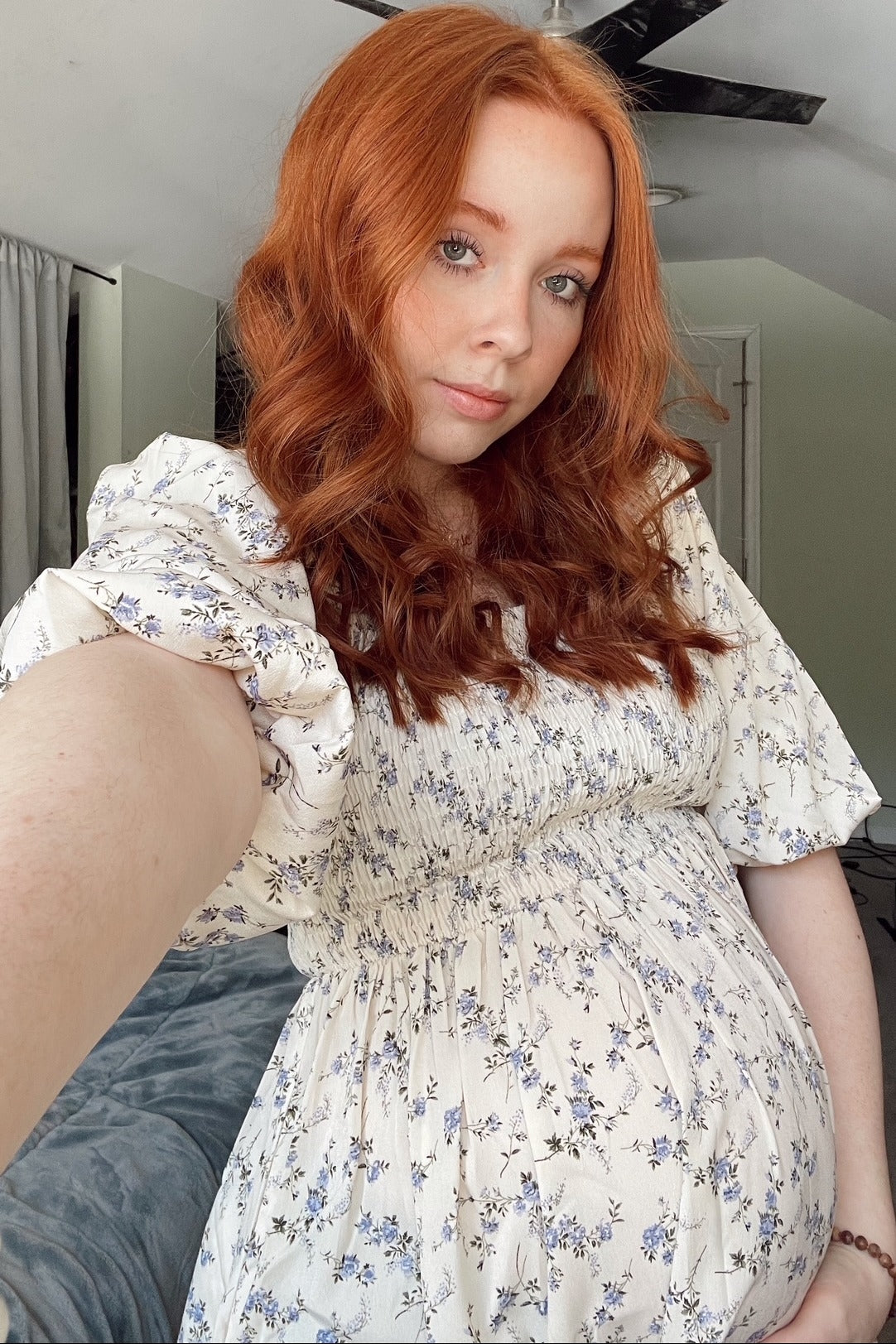 woman wearing a floral print maternity dress with puff sleeves and holding her baby bump