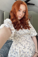 woman wearing a floral print maternity dress with puff sleeves and holding her baby bump