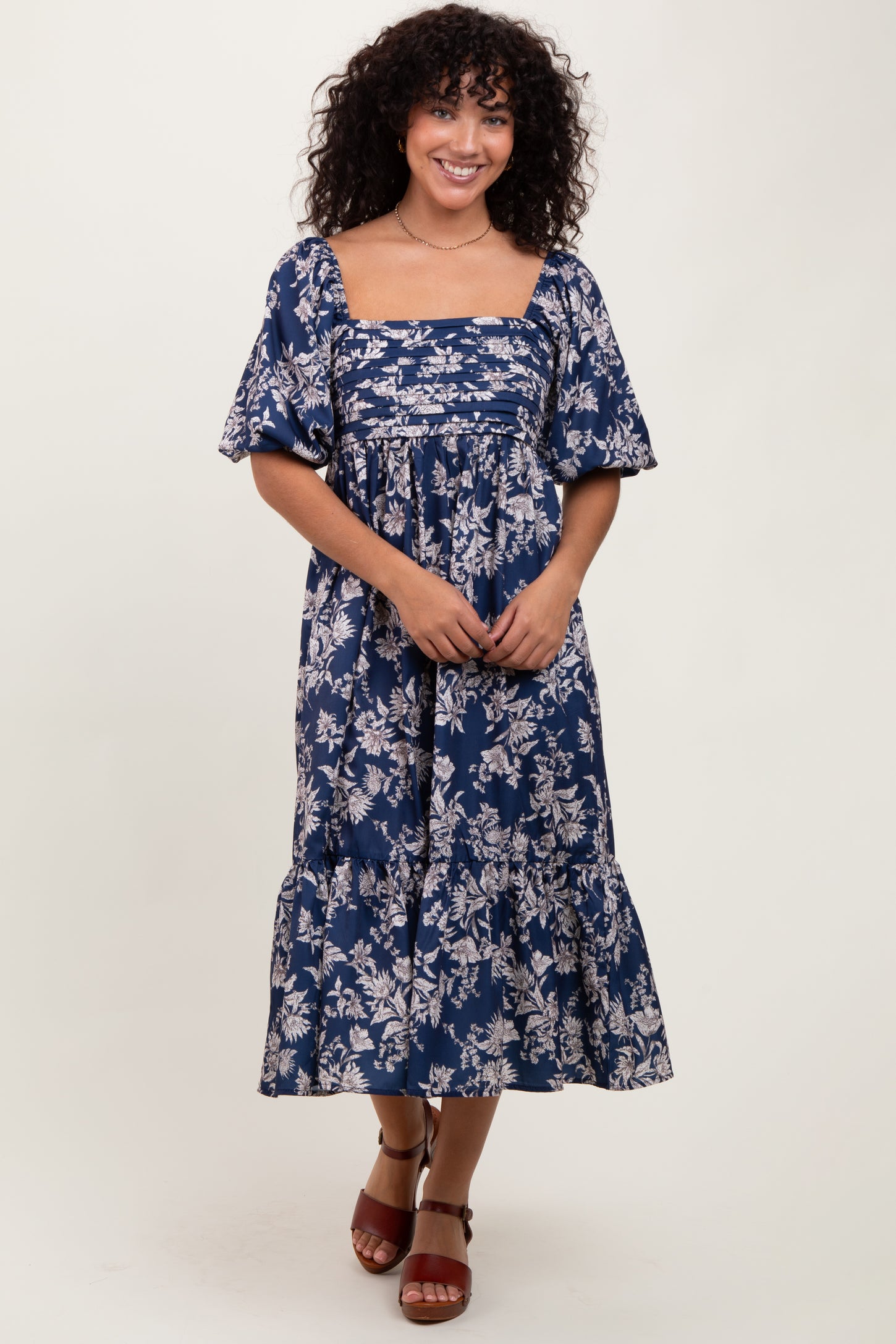 woman wearing a navy blue floral print midi dress with puff sleeves and a tiered hem