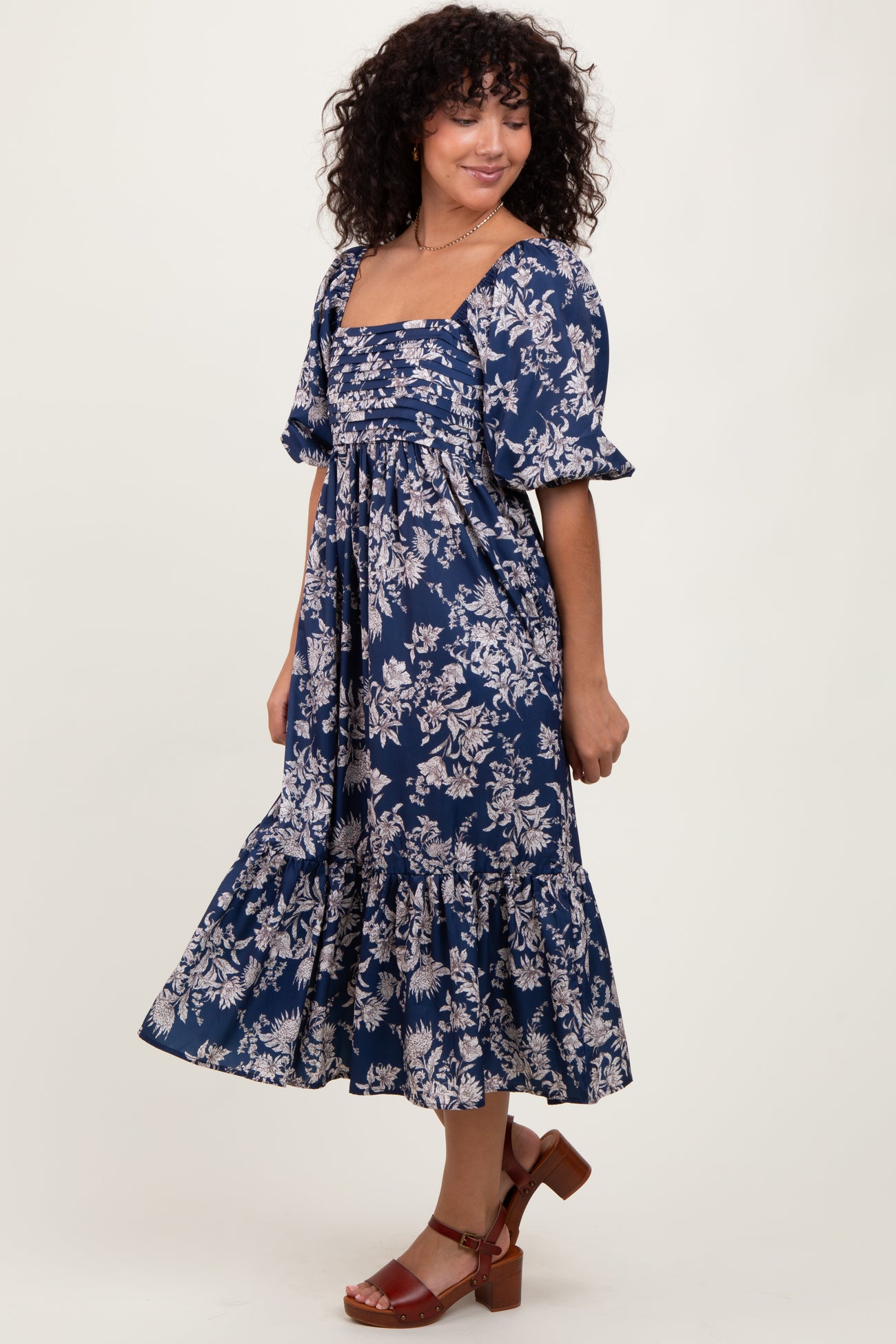 woman wearing a navy blue floral midi dress with puff sleeves and a tiered skirt, smiling and standing in profile