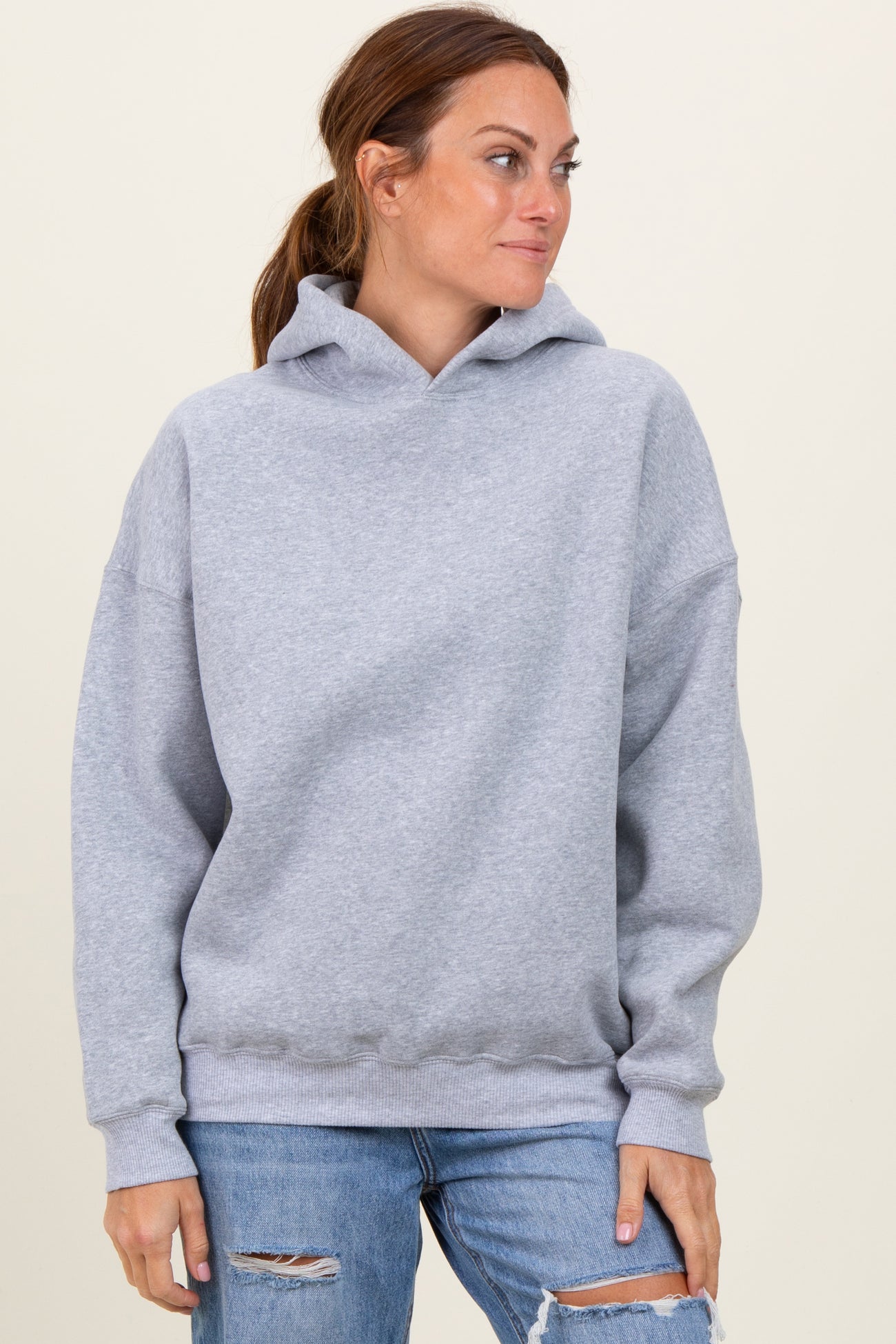 woman wearing a light gray oversized hoodie with a front pocket and long sleeves, paired with ripped jeans