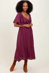 woman wearing a burgundy maxi dress with a front tie and flutter sleeves, paired with brown ankle boots