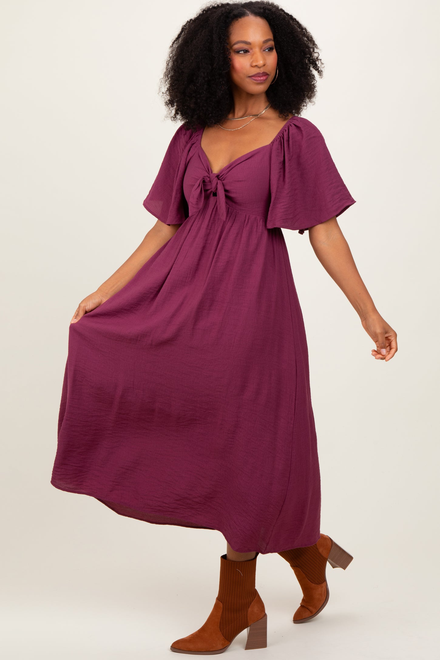 woman wearing a plum midi dress with a tie front and short puff sleeves, paired with brown ankle boots