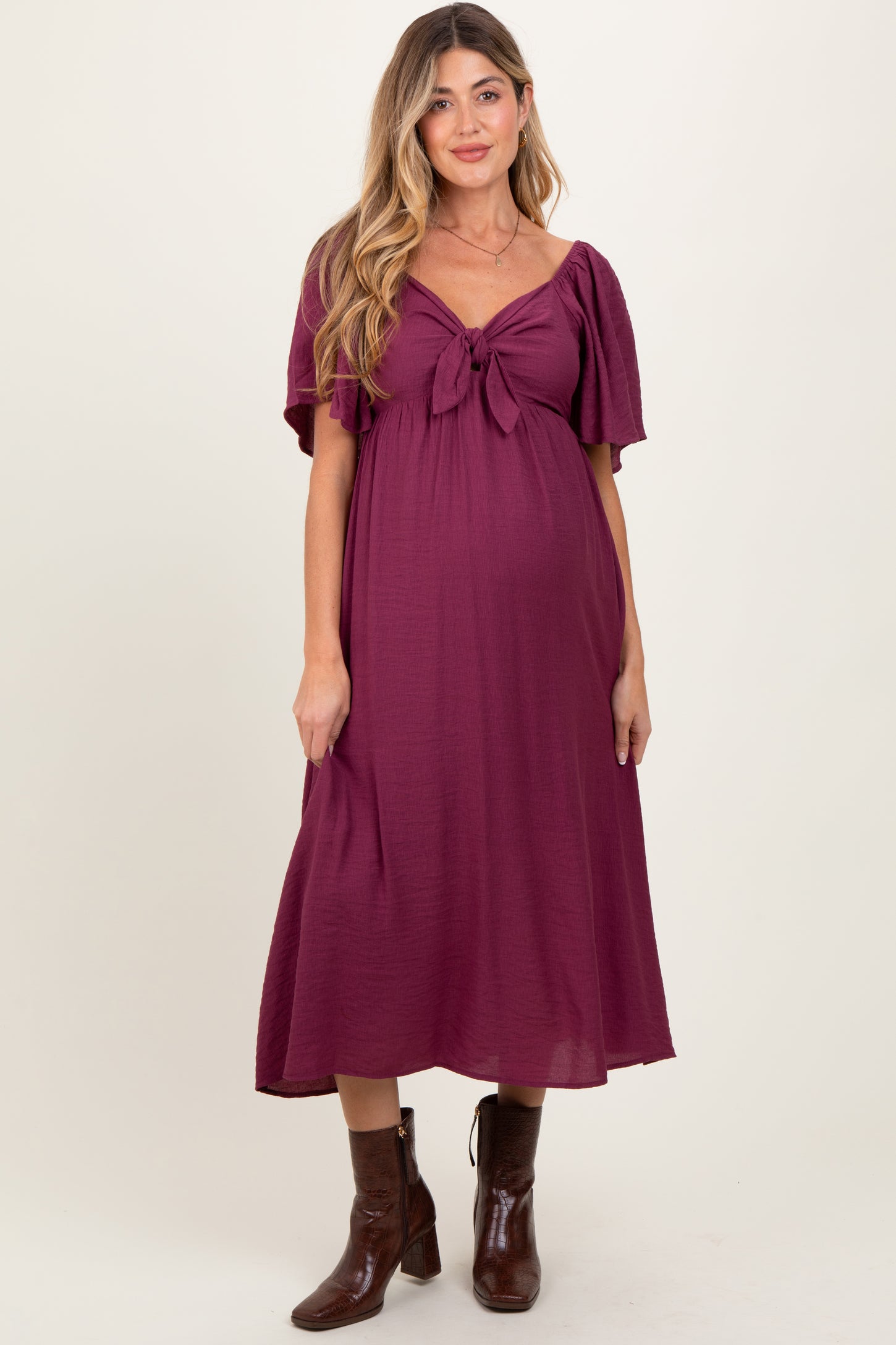 woman wearing a burgundy maternity dress with a front tie detail and flutter sleeves, showcasing a baby bump