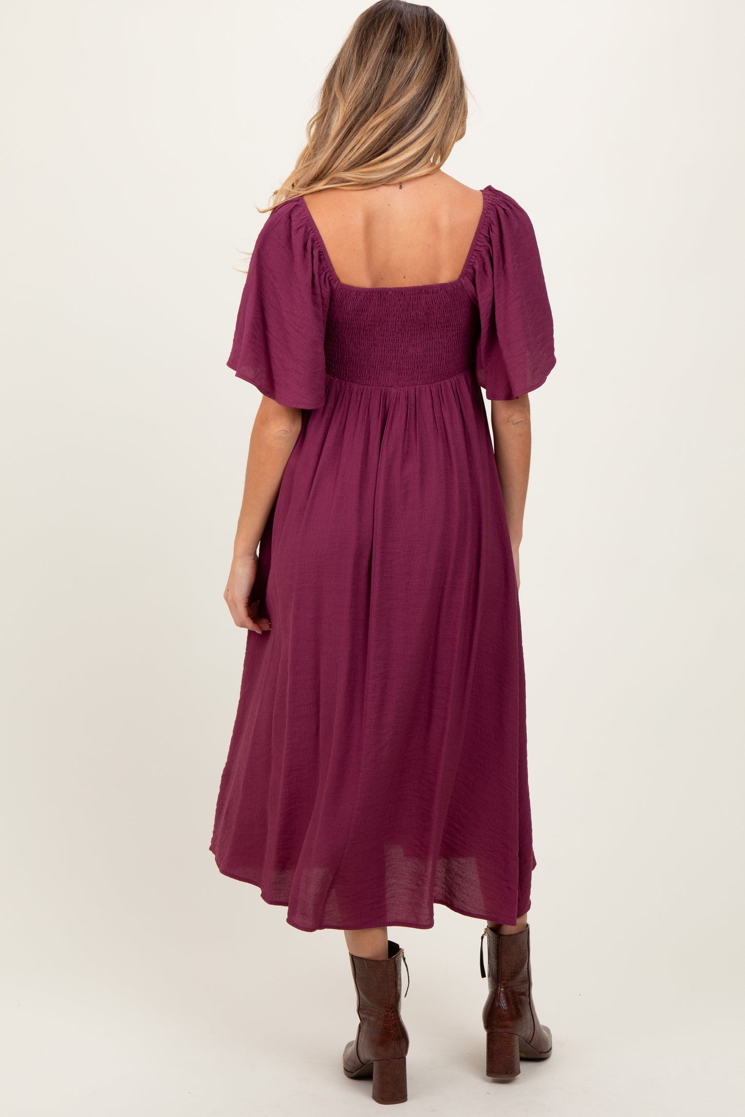 woman wearing a maternity dress in deep magenta with short flutter sleeves and a smocked bodice, showing a flowing skirt