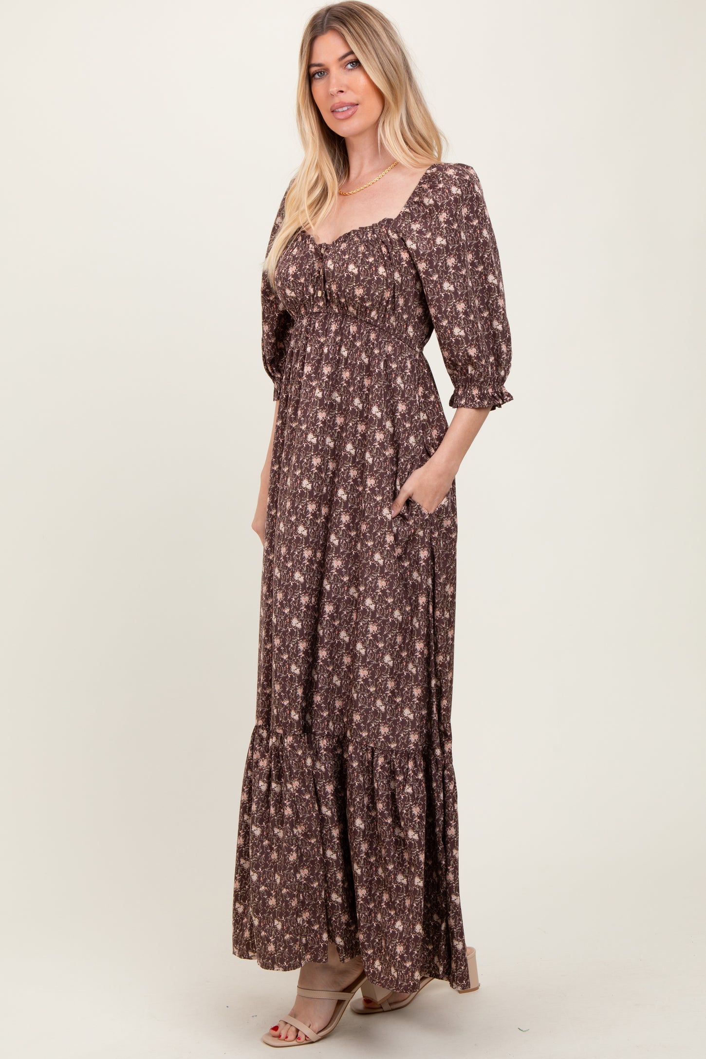woman wearing a brown floral maxi dress with puff sleeves and pockets, standing against a neutral background