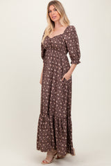 woman wearing a brown floral maxi dress with puff sleeves and pockets, standing against a neutral background