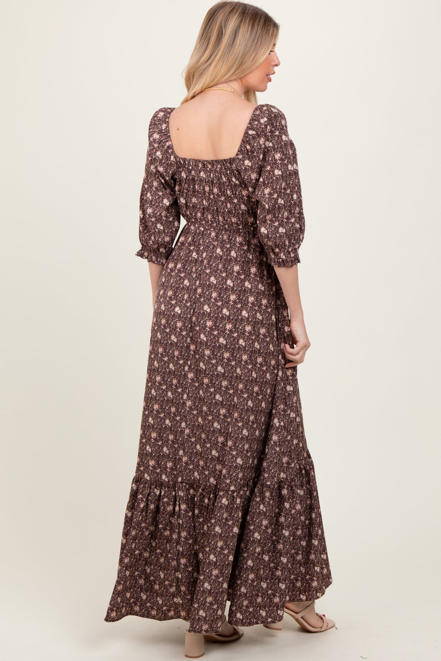 woman wearing a brown floral maxi dress with puff sleeves and a ruffled hem, viewed from the back