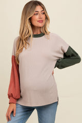 woman wearing a maternity knit sweater with beige body and green and rust long sleeves, showing her baby bump