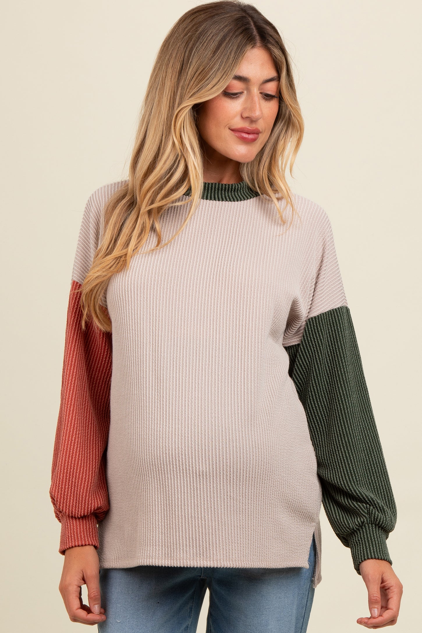 woman wearing a ribbed maternity top with color block sleeves in rust and green, showing her baby bump