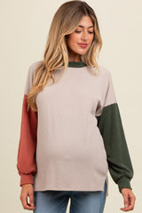 woman wearing a ribbed maternity top with color block sleeves in rust and green, showing her baby bump