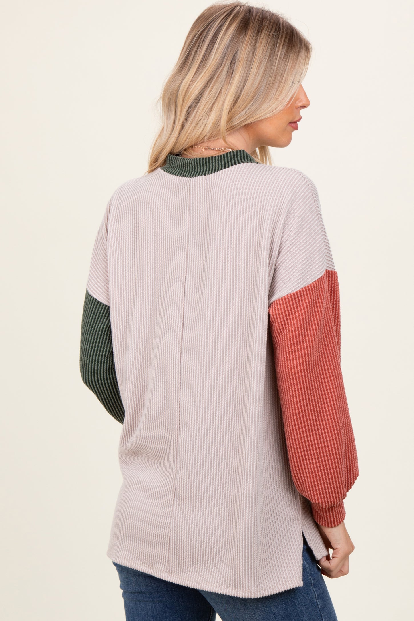 woman wearing a ribbed color-block sweater in beige, green, and rust, viewed from the back
