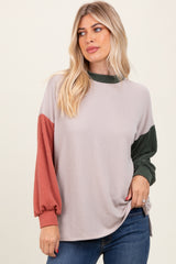 woman wearing a beige ribbed long sleeve top with green and rust colored sleeves, styled with a side knot