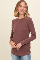 woman wearing a mauve long sleeve ribbed top with a crew neck and relaxed fit, smiling against a light background