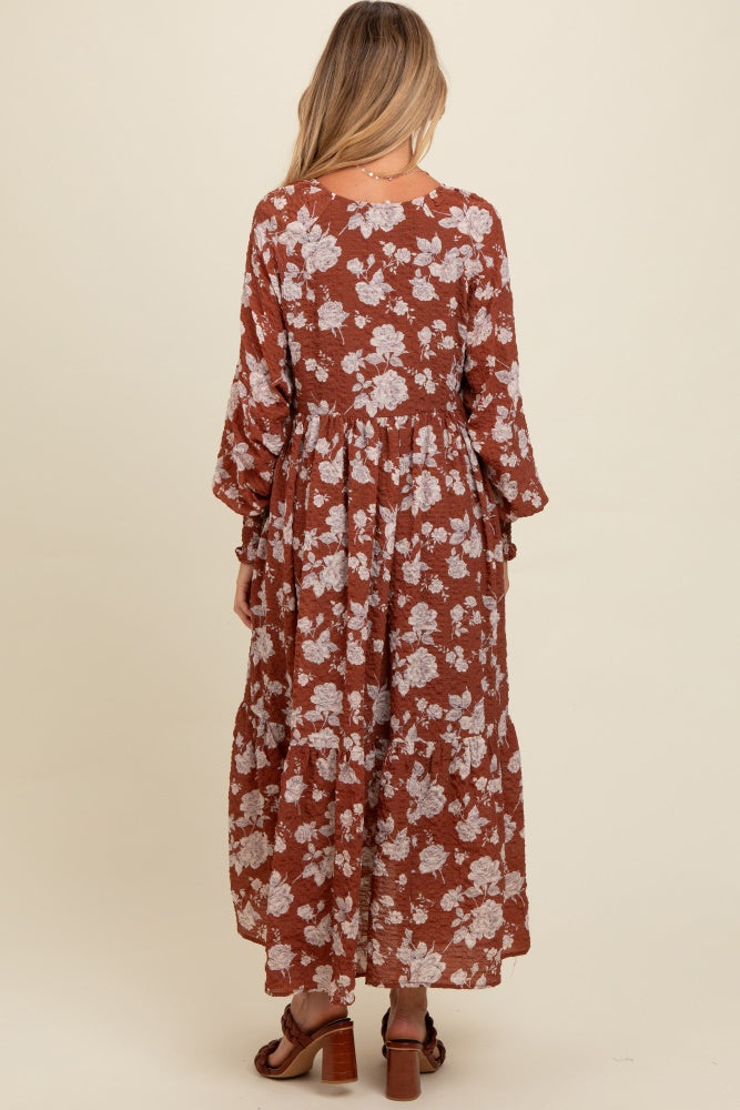 woman wearing a rust-colored floral maternity maxi dress with long sleeves and a tiered skirt, showing a baby bump from behind