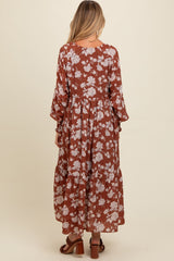 woman wearing a rust-colored floral maternity maxi dress with long sleeves and a tiered skirt, showing a baby bump from behind