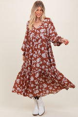 woman wearing a rust floral print maxi dress with long sleeves and a tiered skirt