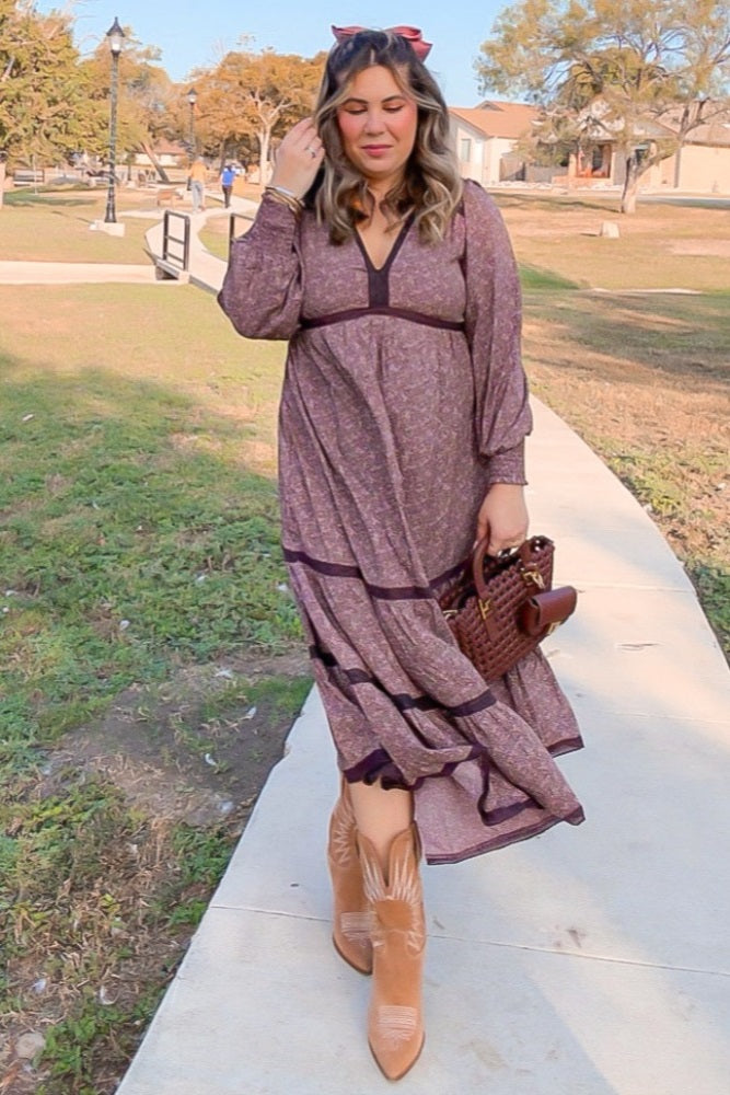 woman wearing a floral long sleeve maxi dress with a tiered skirt and brown ankle boots, holding a handbag while walking