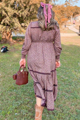 woman wearing a mauve floral maxi dress with tiered detailing and a ribbon in her hair, carrying a small brown handbag