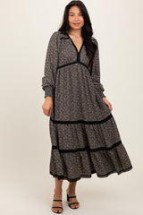 woman wearing a black and floral long sleeve dress with a v-neckline and tiered skirt, standing with one hand on her hip