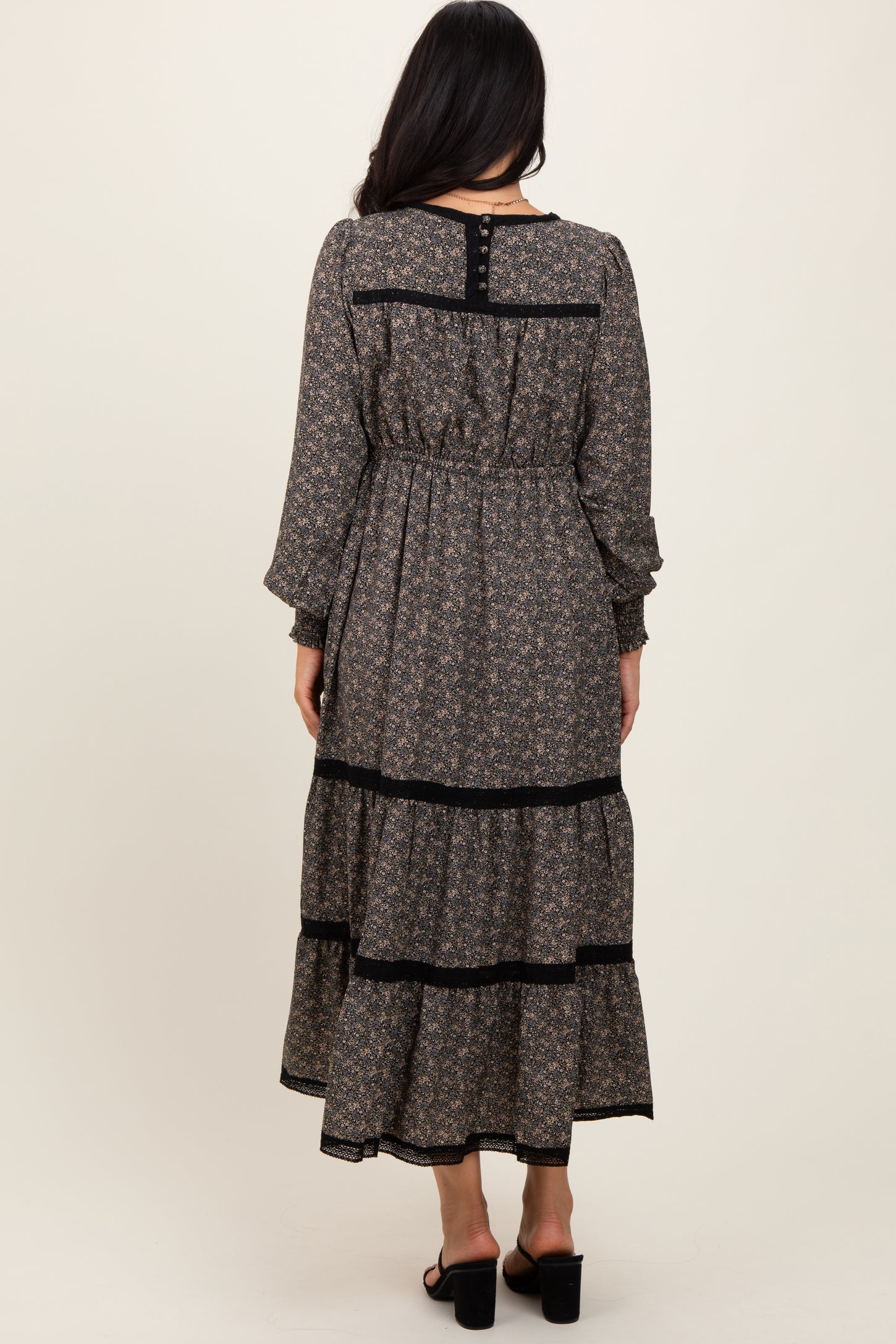 woman wearing a black and floral maxi dress with long sleeves and tiered ruffles, showing the back view
