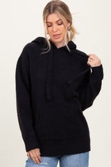 woman wearing a black oversized hooded sweater with a front pocket and ribbed cuffs, styled with light blue jeans