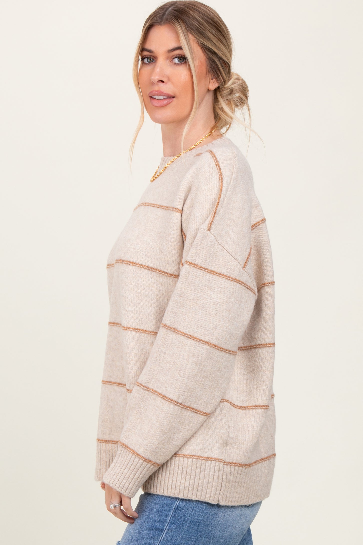 woman wearing a beige striped sweater with gold accents and blue jeans