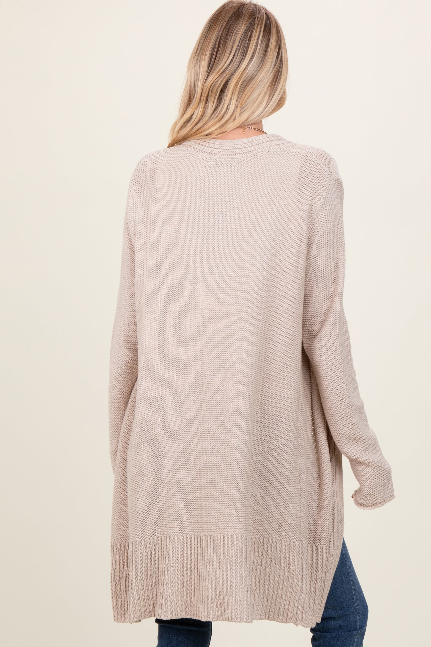 woman wearing a beige long cardigan with a relaxed fit and ribbed detail on the hem, viewed from the back