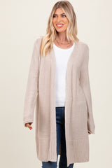 woman wearing a beige long cardigan over a white top and blue jeans, smiling at the camera