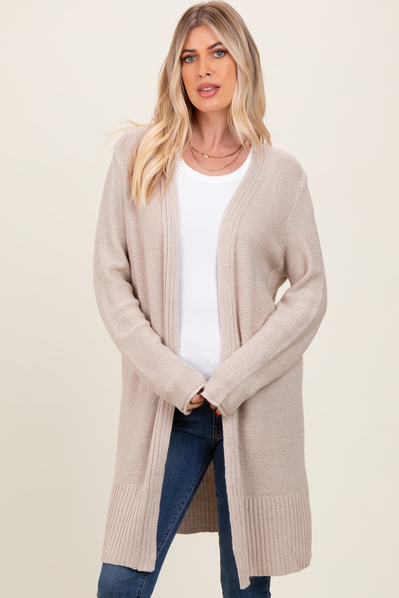 woman wearing a beige long cardigan over a white top and blue jeans