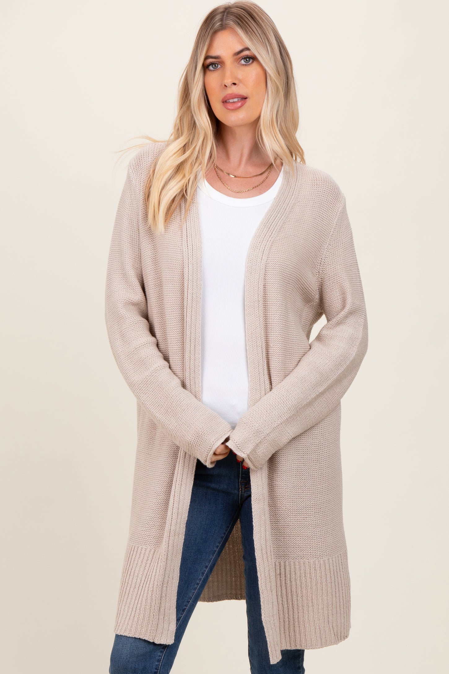 woman wearing a beige long cardigan over a white top and blue jeans