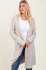 woman wearing a light beige long cardigan over a white top and blue jeans, styled with loose hair