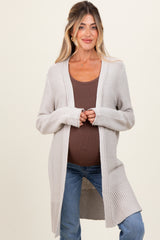 woman wearing a light gray long cardigan over a brown tank top, showing her baby bump, paired with blue jeans