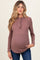 woman wearing a mauve long sleeve maternity top with a ruffle neckline and buttons, showcasing her baby bump