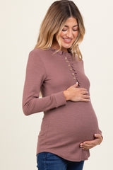 woman wearing a mauve maternity ribbed top with ruffle detail and buttons, showing her baby bump