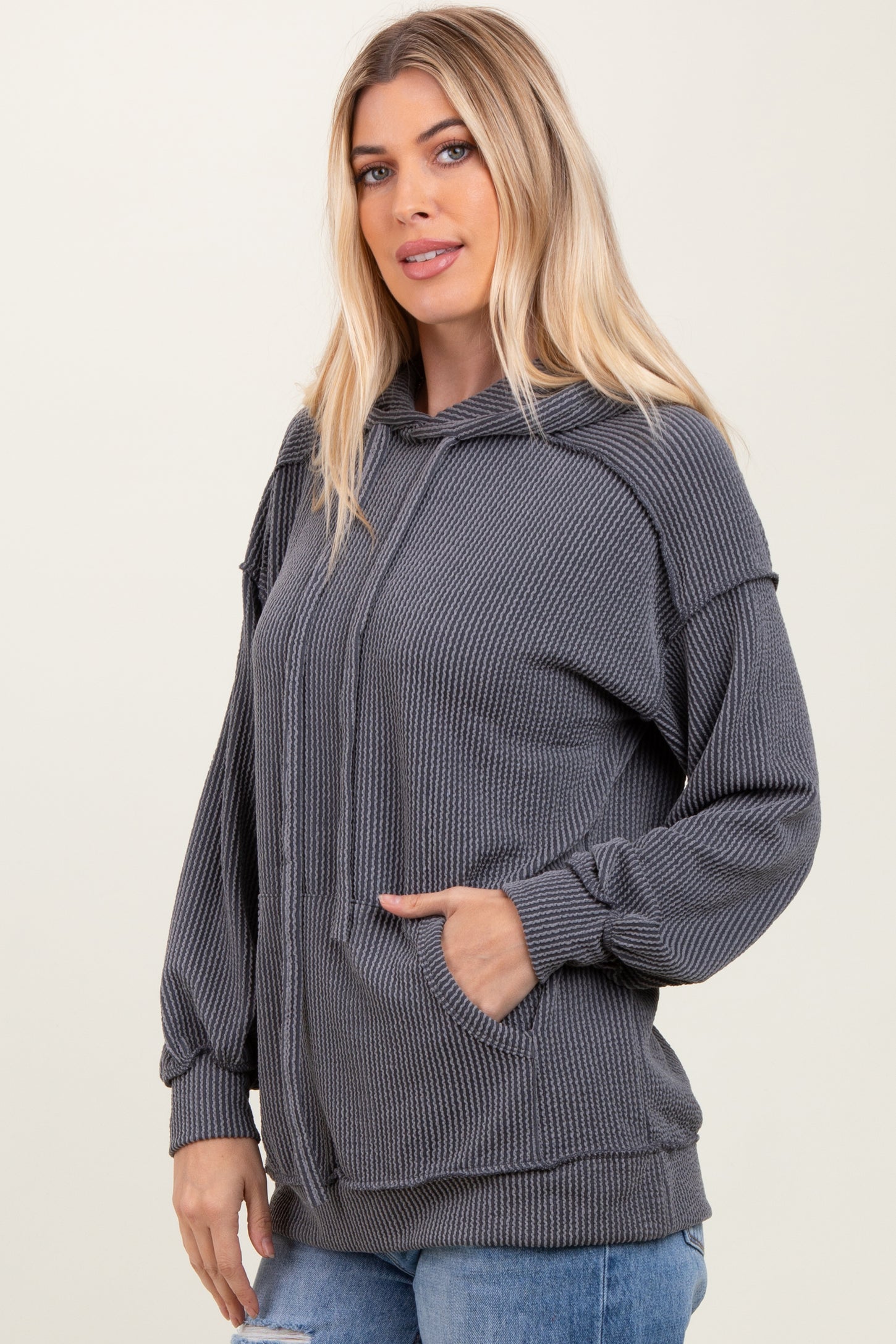 woman wearing a gray ribbed hoodie with a front pocket and relaxed fit, styled with blue distressed jeans