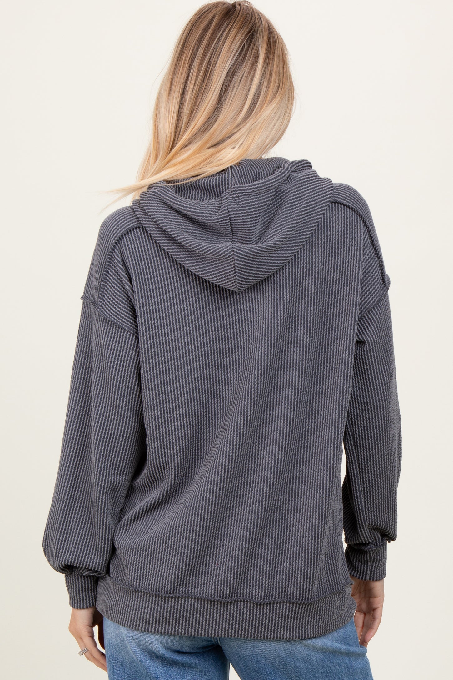 woman wearing a dark gray ribbed hoodie with a relaxed fit and a hood, facing away from the camera