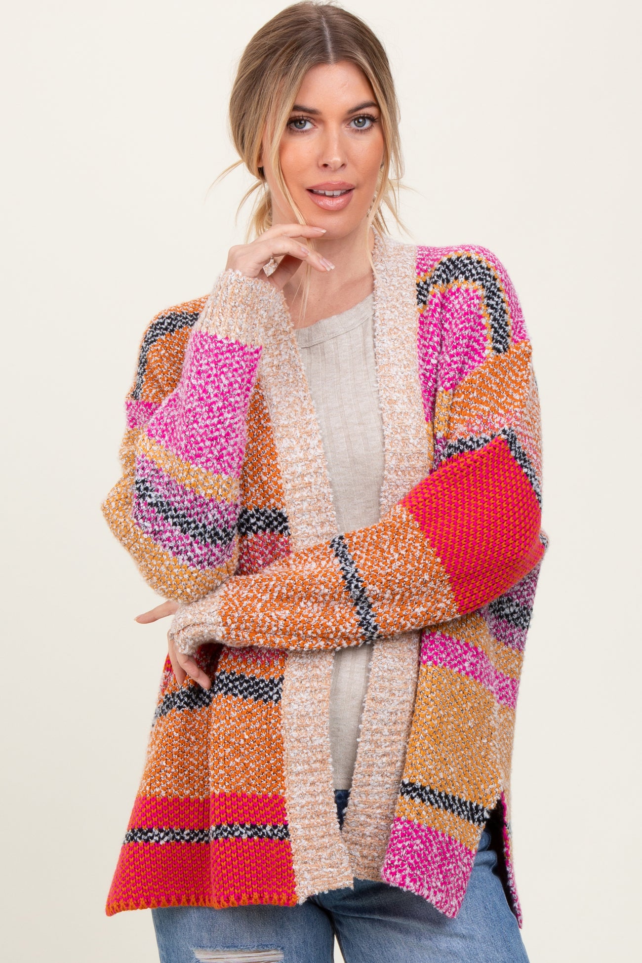 woman wearing a colorful oversized cardigan with pink, orange, and red stripes over a light sweater and jeans