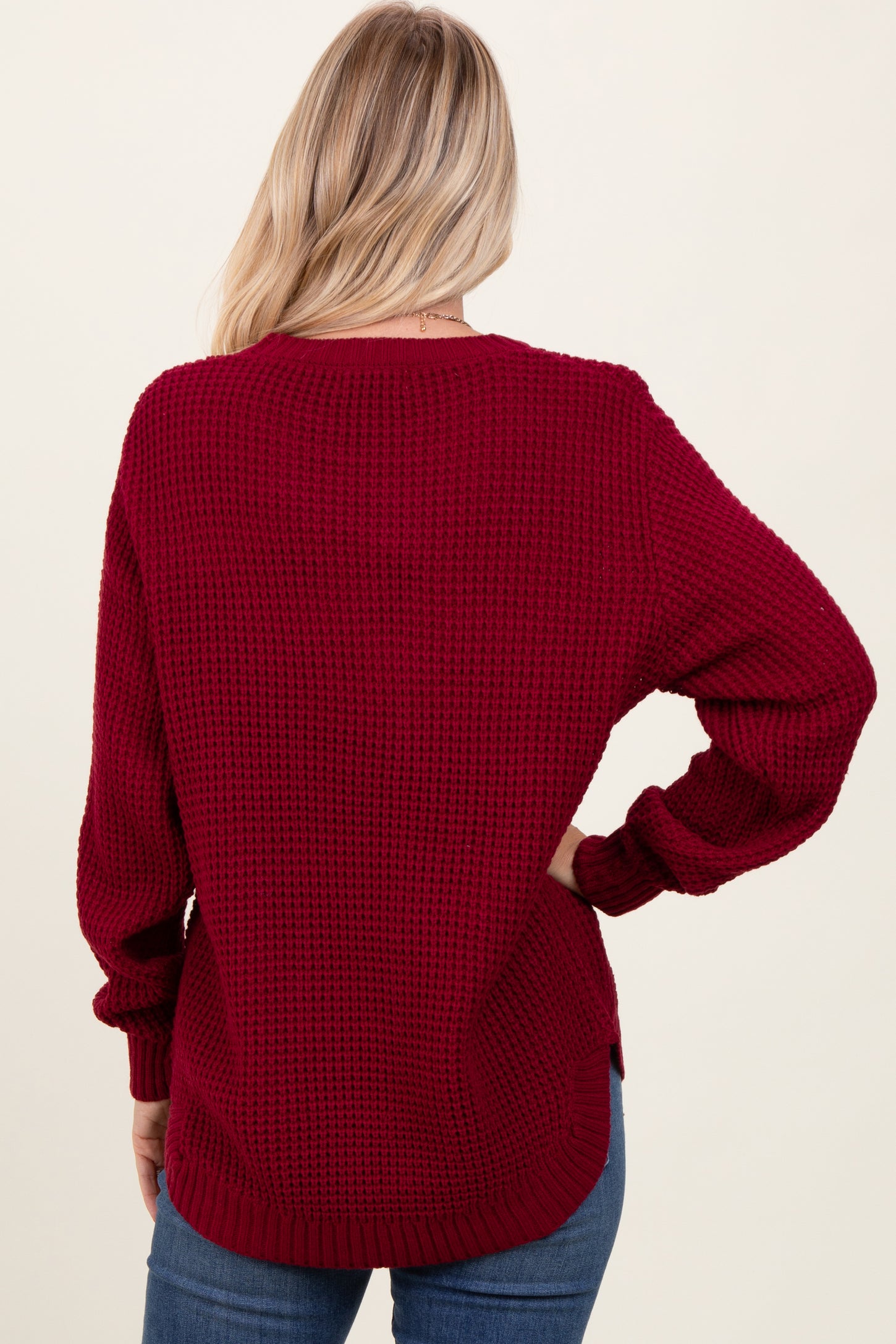 woman wearing a burgundy oversized knitted sweater with a textured pattern and long sleeves, viewed from the back