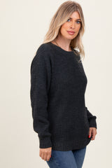 woman wearing a dark gray chunky knit sweater and blue jeans, facing slightly to the side