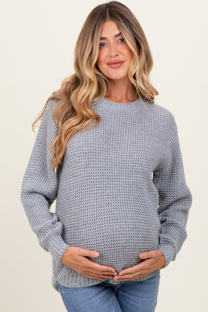 woman wearing a light grey textured maternity sweater and holding her baby bump
