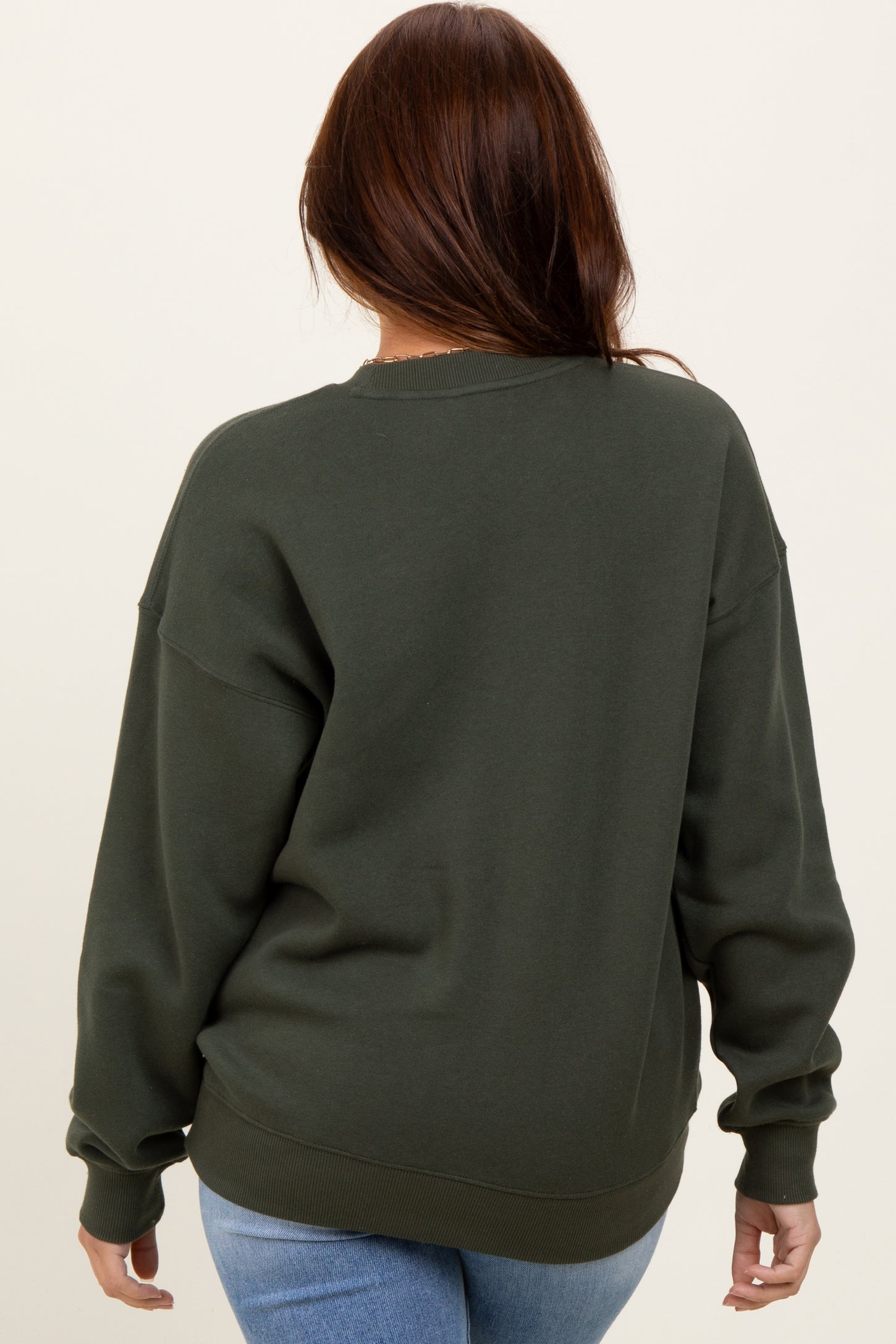 woman wearing a dark green oversized sweatshirt, seen from the back with ribbed cuffs and hem