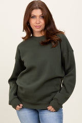 woman wearing a dark green oversized sweatshirt with ribbed cuffs and relaxed fit, paired with light blue jeans