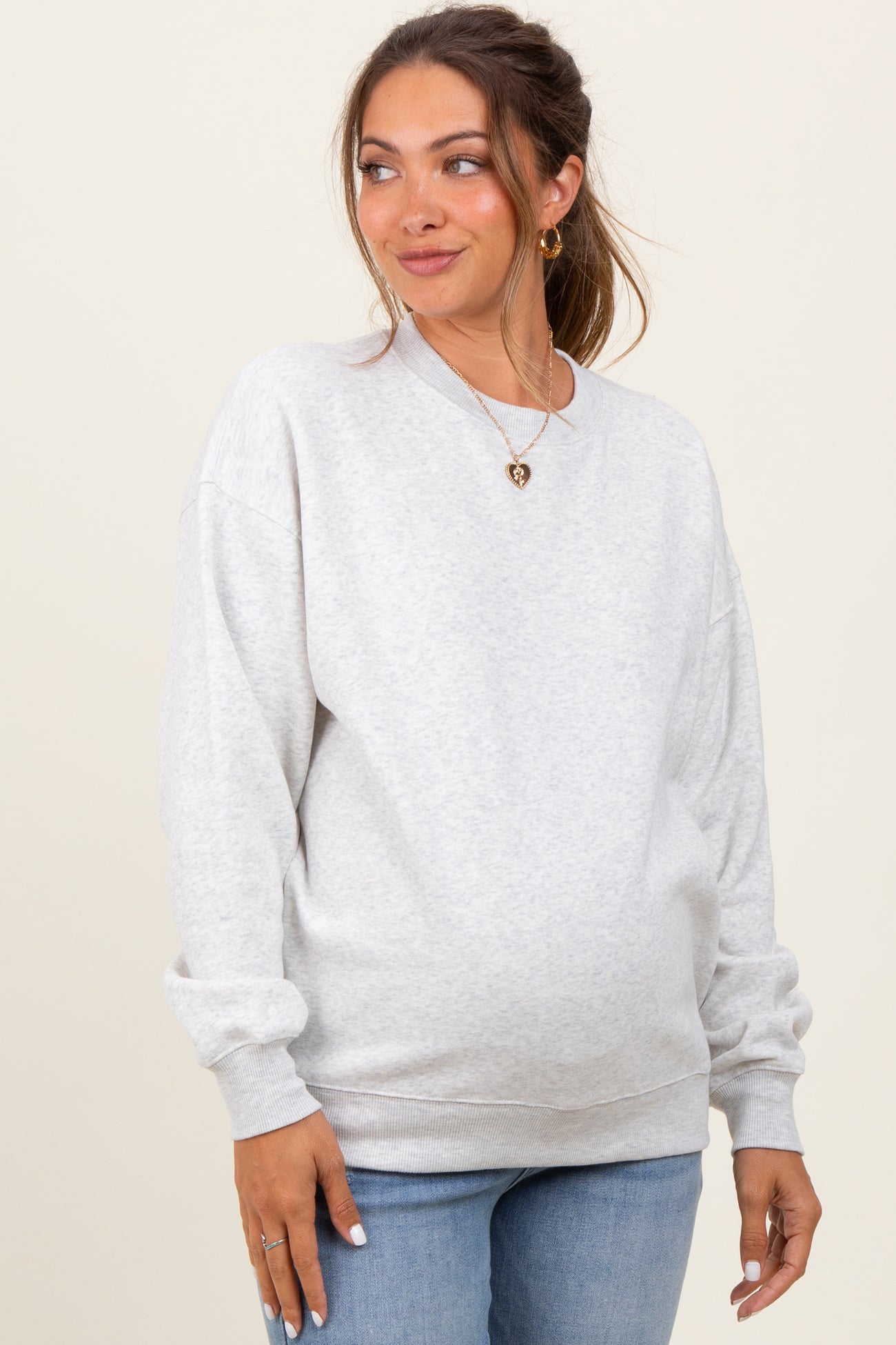 woman wearing a light grey oversized maternity sweatshirt and blue jeans with a visible baby bump